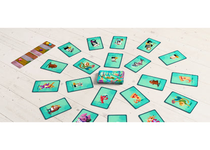 Een set kleurrijke, geïllustreerde Dierenshow-speelkaarten van Haba Spellen ligt in een cirkel op een witte houten vloer, met de kaartendoos in het midden en een rij tegels aan de zijkant, geïnspireerd op kinderspel op een bosfestival.