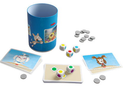 Een Dobbelbeker - Woef Woef container van Haba Spellen heeft een blauw cilindervormig ontwerp met dierenillustraties, omringd door kleurrijke dobbelstenen, grijze lopers en speelkaarten met cartoondieren op een witte achtergrond.