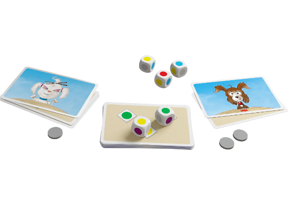 Drie stapeltjes dierenkaarten, drie veelkleurige dobbelstenen en vier grijze lopers uit het Dobbelbeker - Woef Woef bordspel van Haba Spellen zijn gerangschikt op een wit oppervlak, wat een leuke kaartspelopstelling suggereert.